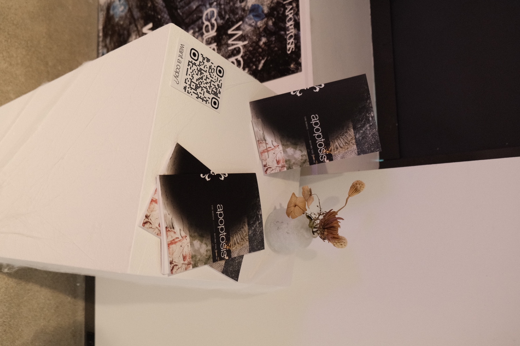 Copies of the Apoptosis book displayed with dried flowers at the exhibition
